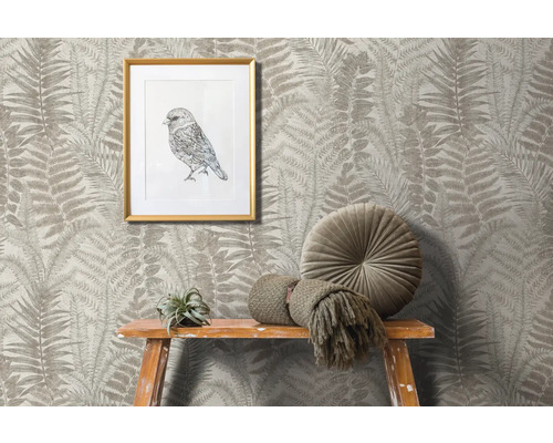 Scen med tapet med ormbunksmönster, inramad fågelbild, rund kudde och dekoration på en träpall