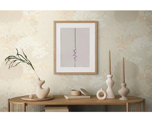 Dekorativ scen med en inramad bild, vaser och ljus på ett träbord framför en mönstrad tapet.