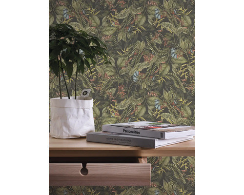 Närbild av en vägg med en djungeltapet med växter och blommor, kompletterad med en växt i en kruka och böcker på ett träbord.