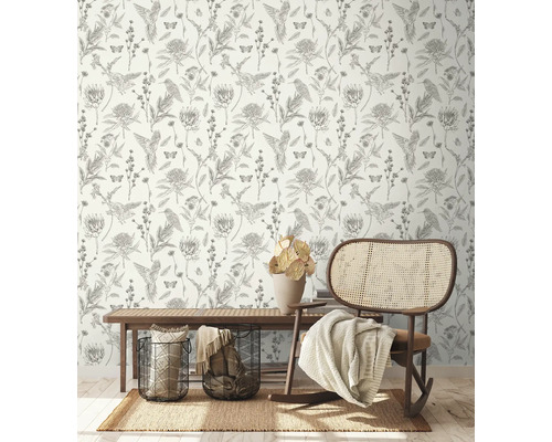 Dekorativt rum med tapet med fågel-, blom- och fjärilsmönster, en matta, en bänk, korgar och en gungstol.