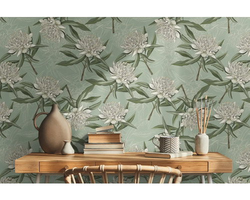 Scen med en bordsskiva i trä framför en väggtapet med blommönster, dekorerad med en vas, staplar av böcker och en kopp