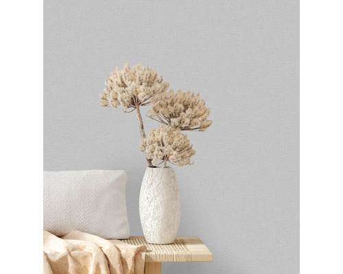 Dekorativ vas med torkade blommor på ett bord med kuddar mot en strukturerad vägg