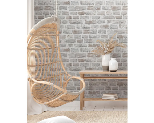 Hängfåtölj i rotting i ett ljust, vänligt rum med tapet i tegelimitation