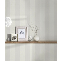 Interiörbild av ett rum med randig tapet, dekorerat med en trähylla, fotoramar och en lampa