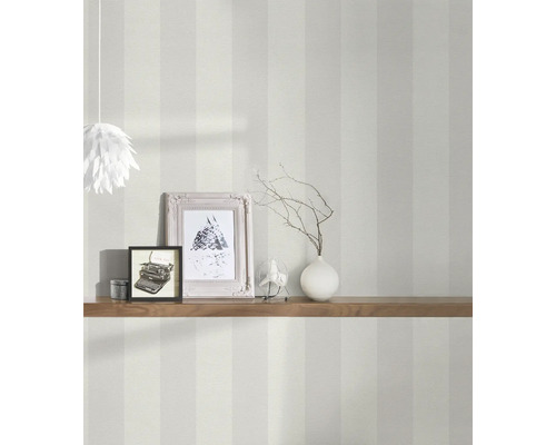 Interiörbild av ett rum med randig tapet, dekorerat med en trähylla, fotoramar och en lampa