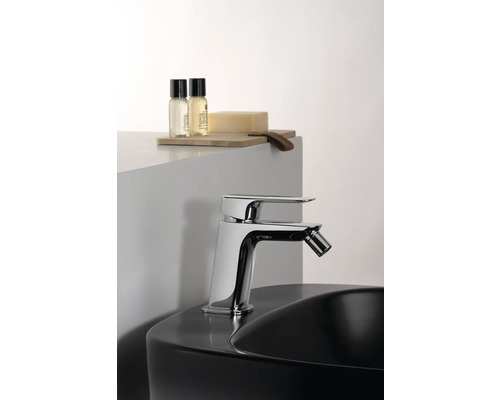 Blankpolerad bidéblandare på ett svart handfat med vårdprodukter på en trähylla