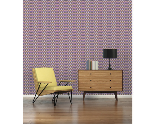 Scen med fåtölj, byrå, lampa och mönstrad tapet.