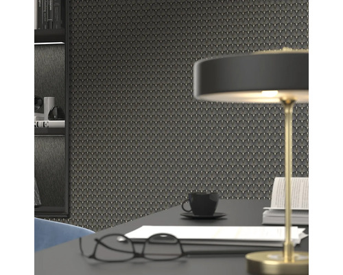 Närbild av en vägg med tapeter i art déco-stil, kompletterad med ett skrivbord med en lampa, glasögon, en kaffekopp och böcker.