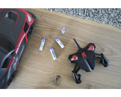 Leksaksbil, fjärrkontroll och batterier på ett trägolv