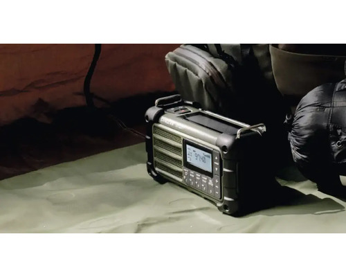 Bärbar nödradio med solpanel och handvev bredvid en ryggsäck och en sovsäck i tältet