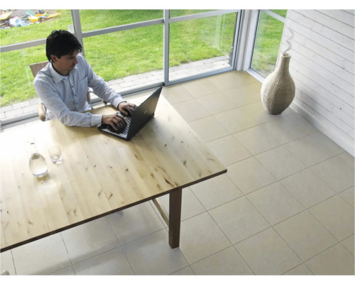 Ljust rum med klinkergolv, träbord och person som arbetar på en bärbar dator