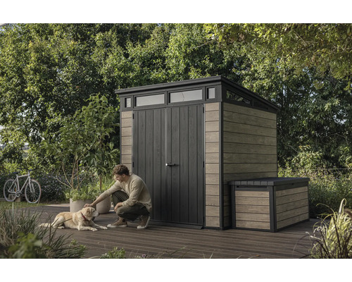 Trädgårdsscen med redskapsbod och förvaringslåda, man klappar hund