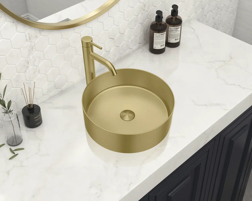 På ett handfat står ett bänkskåpshandfat i guldfärg med armatur