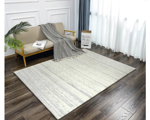 Vardagsrum med soffa, prydnadskudde och mönstrad matta på trägolv.