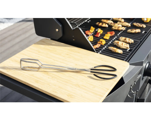 Grillscen med grilltång, skärbräda, grillmat