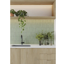 Köksscen med diskho, blandare, bänkskiva, grön kakelvägg och krukväxter