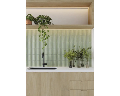 Köksscen med diskho, blandare, bänkskiva, grön kakelvägg och krukväxter