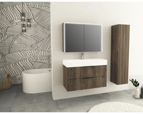 Badrum med tvättställ, spegelskåp och högskåp i trälook framför en vägg med bladmönster