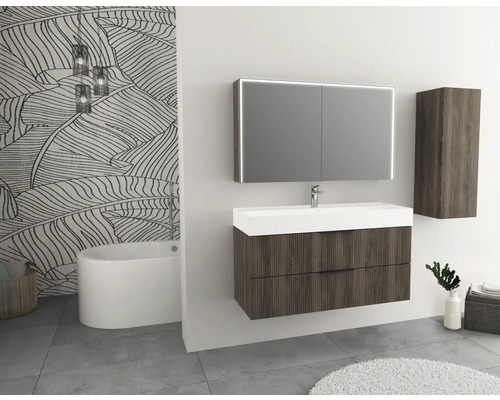 Badrum med tvättställsskåp, spegelskåp och högskåp i trälook samt badkar framför en mönstrad vägg