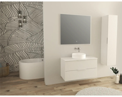 Ljust badrum med tvättställsskåp, tvättställsskål, spegel, högskåp och badkar mot en mönstrad vägg