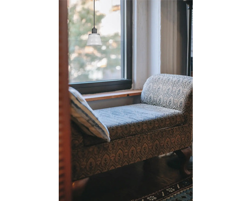 Scen med en lampa, en stoppad bänk och en kudde framför ett fönster. Stilren och mysig interiör.