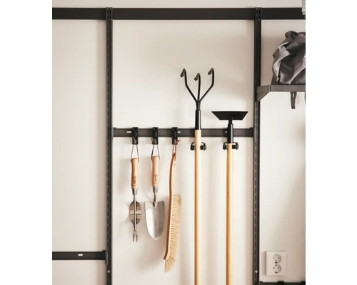 Trädgårdsredskap hänger på ett väggfäste med krokar.