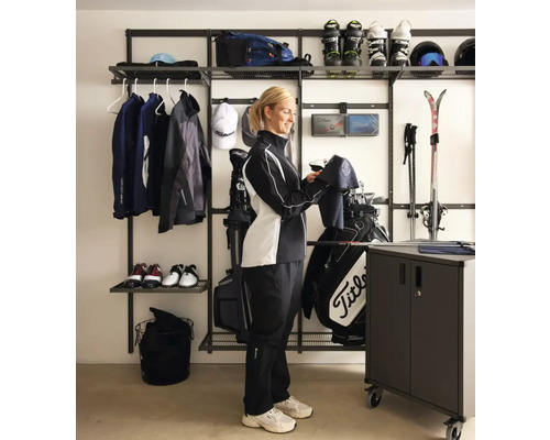 Organiserat förvaringssystem för sportutrustning i ett garage med hyllor, hängare och en kvinna som kontrollerar sin golfutrustning.