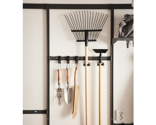 Trädgårdsredskap upphängda på en väggskena, inklusive kratta, spade, sopborste och kultivator