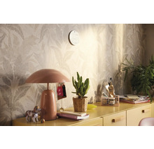 Dekorativt rum med mönstrad tapet, bordslampa och diverse dekorationer på ett gult skåp.