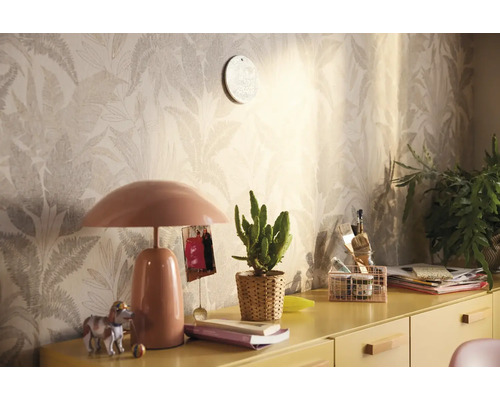 Dekorativt rum med mönstrad tapet, bordslampa och diverse dekorationer på ett gult skåp.