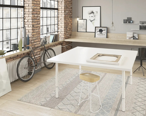 Ljust rum med stort fönster, ateljébord, pall och dekorationer.