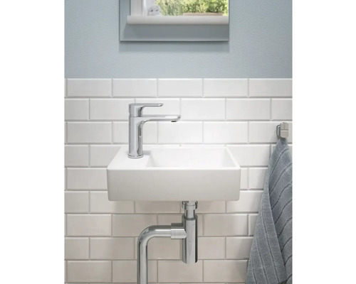 Litet badrumshandfat med blandare och vattenlås framför en vitkaklad vägg