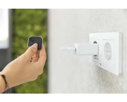 En hand håller en fyrkantig spårare medan en laddare är ansluten till ett uttag