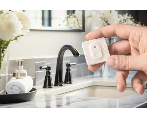 Hand som håller en vattenläckagedetektor i ett badrum med handfat och kran