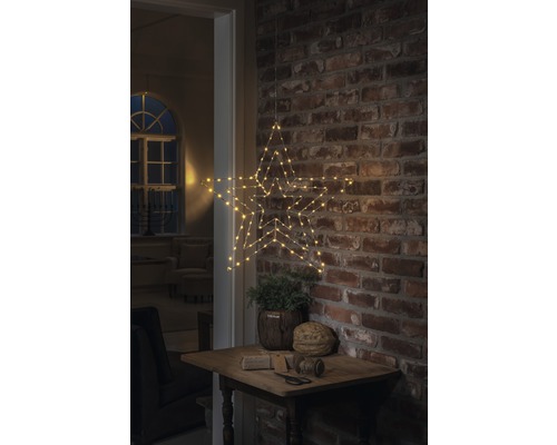 Dekorativ stjärna med LED-belysning, hängande på en tegelvägg ovanför ett litet bord med dekoration.