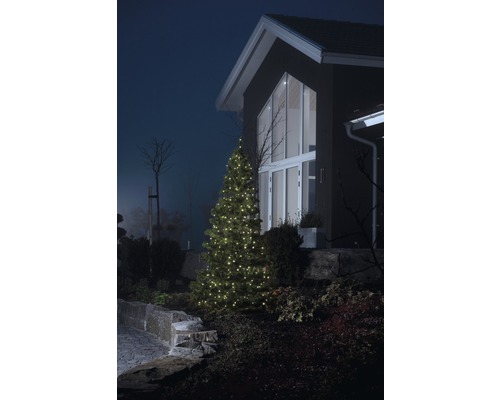 Upplyst julgran framför ett bostadshus i trädgården.