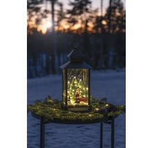 Dekorativ lykta med jultomte, julgranar och belysning på ett bord