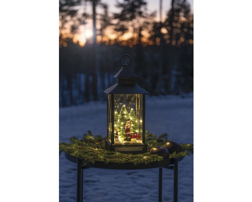 Dekorativ lykta med jultomte, julgranar och belysning på ett bord