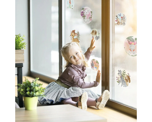 Flicka leker med fönsterdekaler med djurmotiv på en fönsterruta.