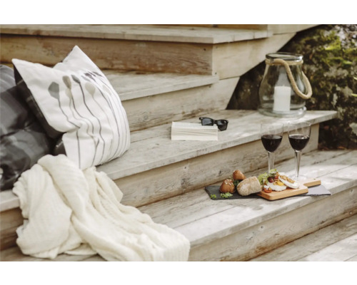 Mysig scen på en trätrappa med kuddar, filt, drycker, mat, bok, solglasögon och en lykta