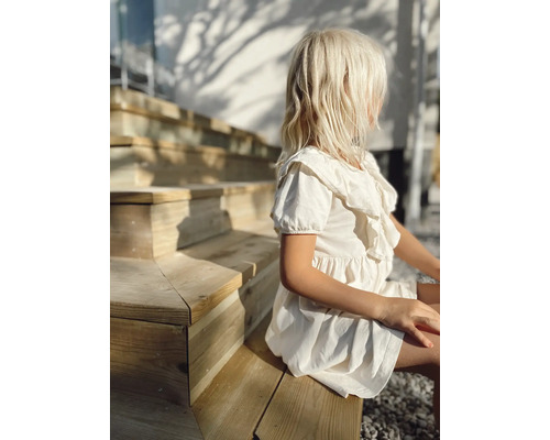 Flicka sitter på en trätrappa och bär en klänning