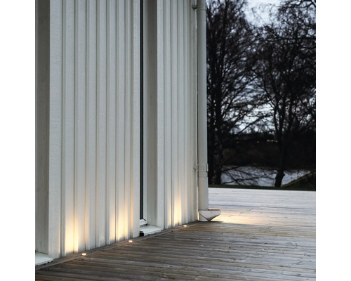 Husvägg med infällda markstrålkastare som lyser upp trägolvet