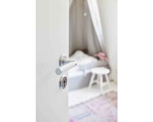 Inbjudande blick genom en öppen dörr in i ett ljust sovrum med säng och pall.