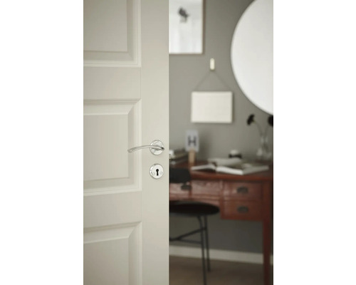 Öppen vit innerdörr med silverfärgat dörrhandtag och nyckelhål, utsikt över ett skrivbord i ett rum