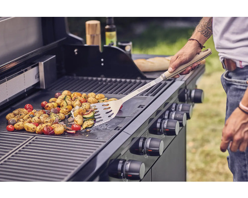 Grönsaker tillagas på en gasolgrill med stekspade.