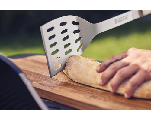 Grillspade i rostfritt stål skär bröd på en träbräda.