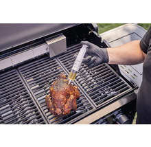 En person injicerar vätska med en spruta i en grillad kyckling på en grill.