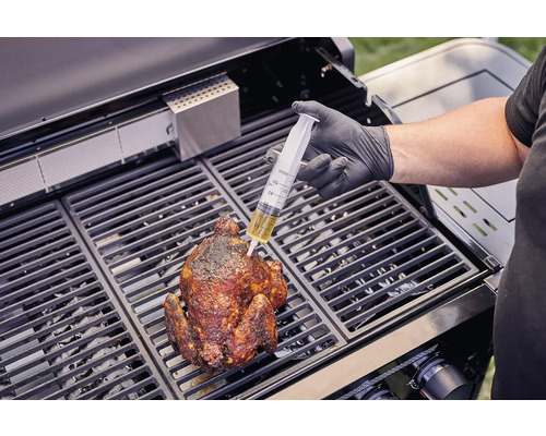 En person injicerar vätska med en spruta i en grillad kyckling på en grill.