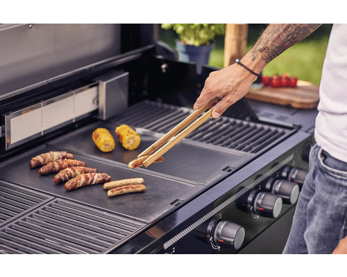 Man grillar korvar och majskolvar på en grill