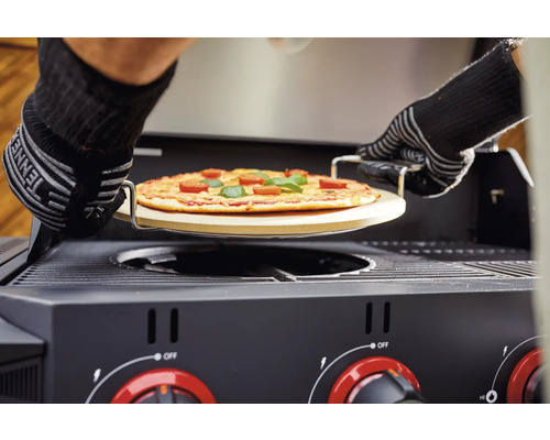 Pizza på en pizzasten skjuts in i en gasolgrill